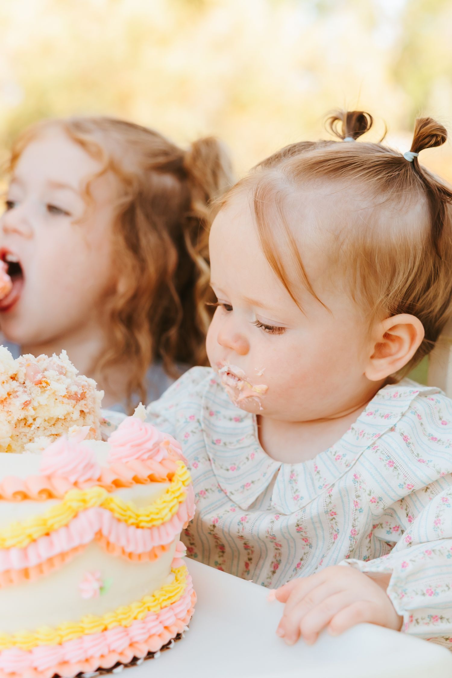 A toddler eagerly leans forward to blow out birthday candles on a pink and orange frosted cake.