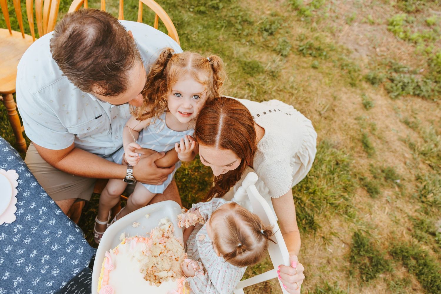 A group sits together on grass while looking at a small object during a sunny outdoor gathering.