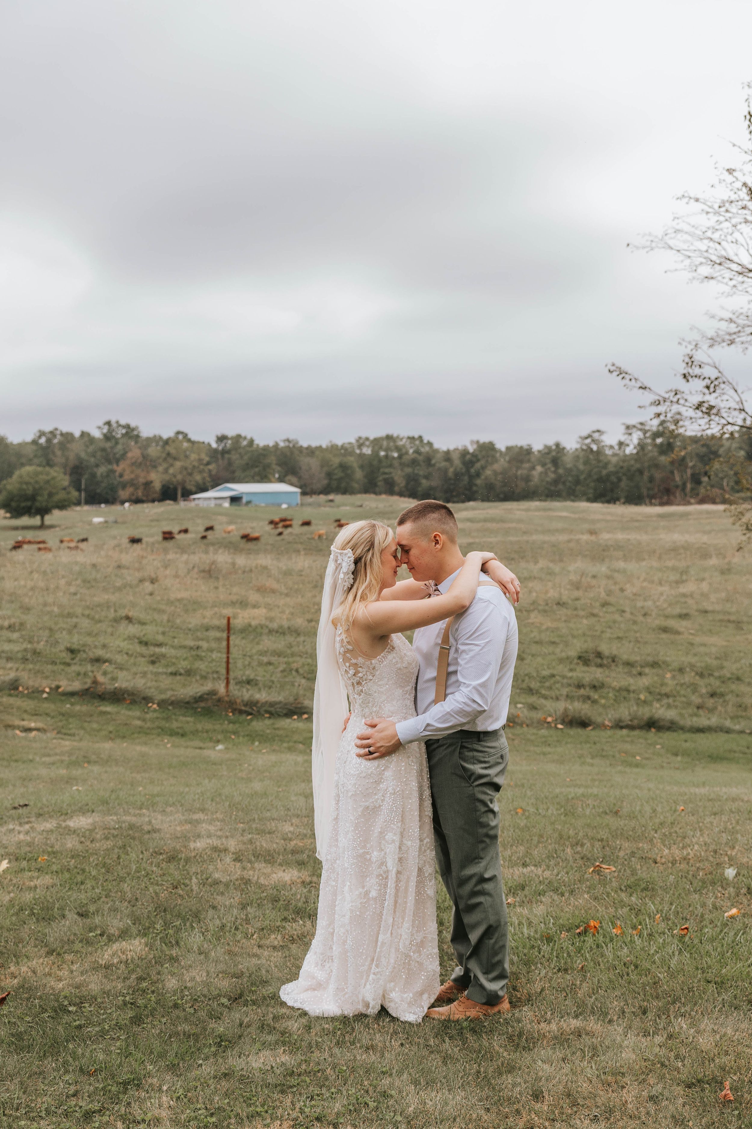 A couple in wedding attire embraces in a serene countryside setting.