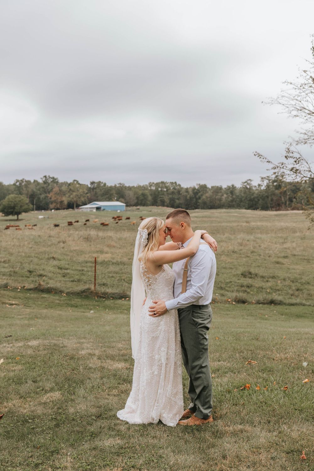 A couple in wedding attire embraces in a serene countryside setting.