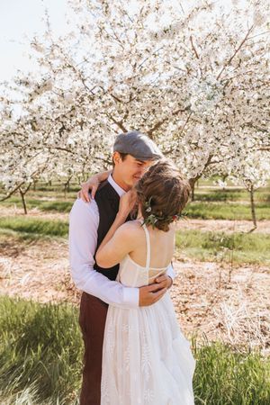 A couple embraces under blooming cherry blossom trees in springtime.