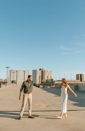 A couple dances playfully on an urban rooftop with city buildings in the background.