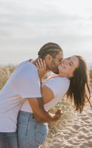 A couple shares a romantic kiss on a sandy beach during golden hour.