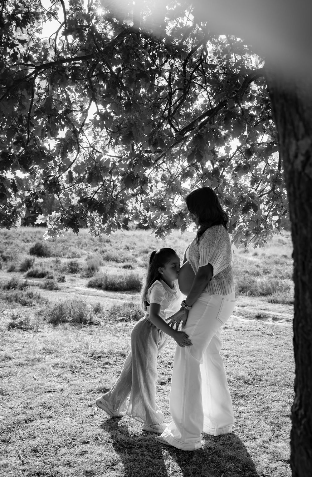 Black and white outdoor photoshoot under a tree with sunlight filtering through branches.