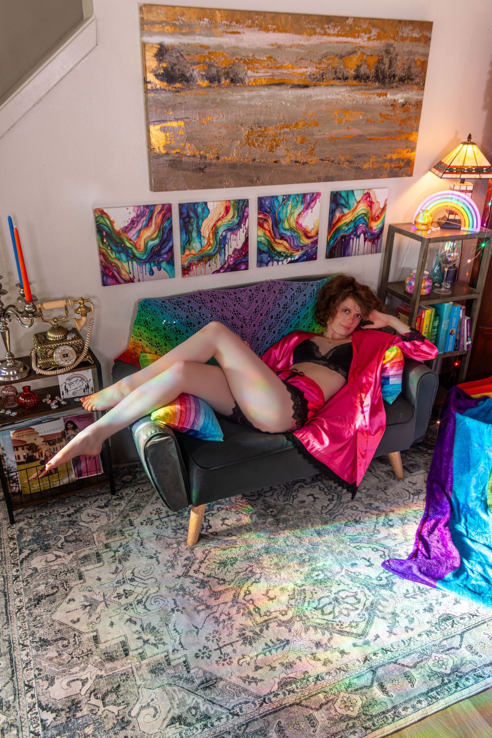 Woman in pink robe reclining on black sofa surrounded by colorful rainbow artwork and decor.