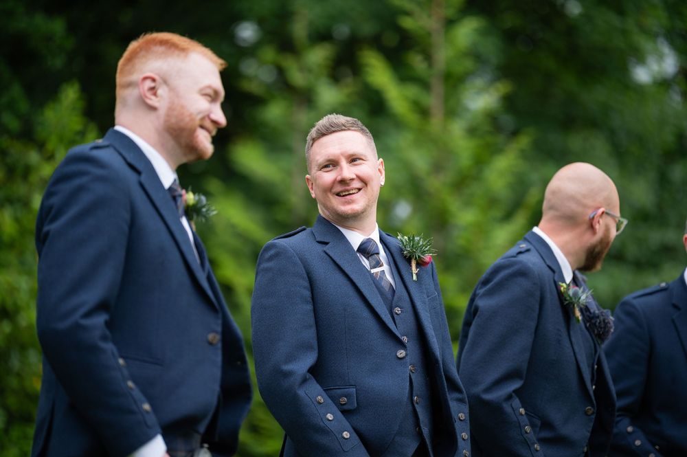 Groomsmen laughing together while wearing matching navy suits and traditional Scottish kilts.