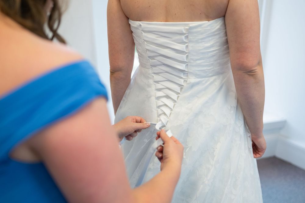 Close-up view of white wedding dress lacing detail being tied in the back.
