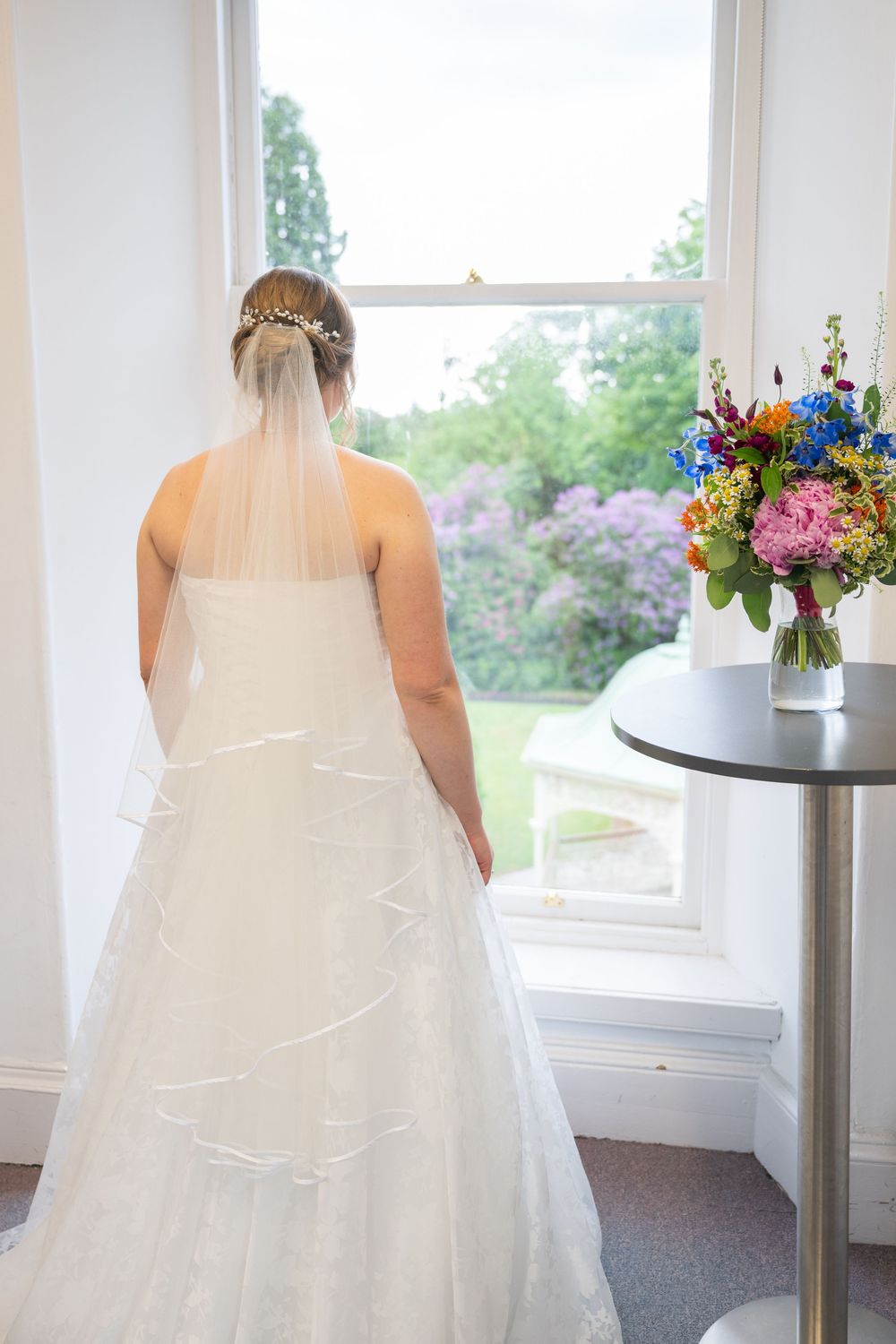 Back view of a wedding dress with detailed lace train against bright windows.