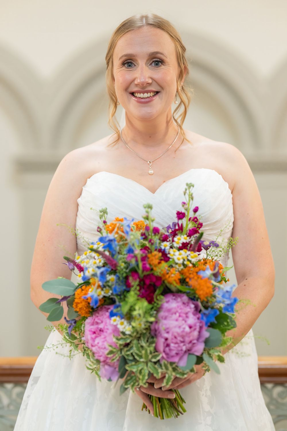 Bride holding vibrant multicolored wedding bouquet with pink, orange, and blue flowers.