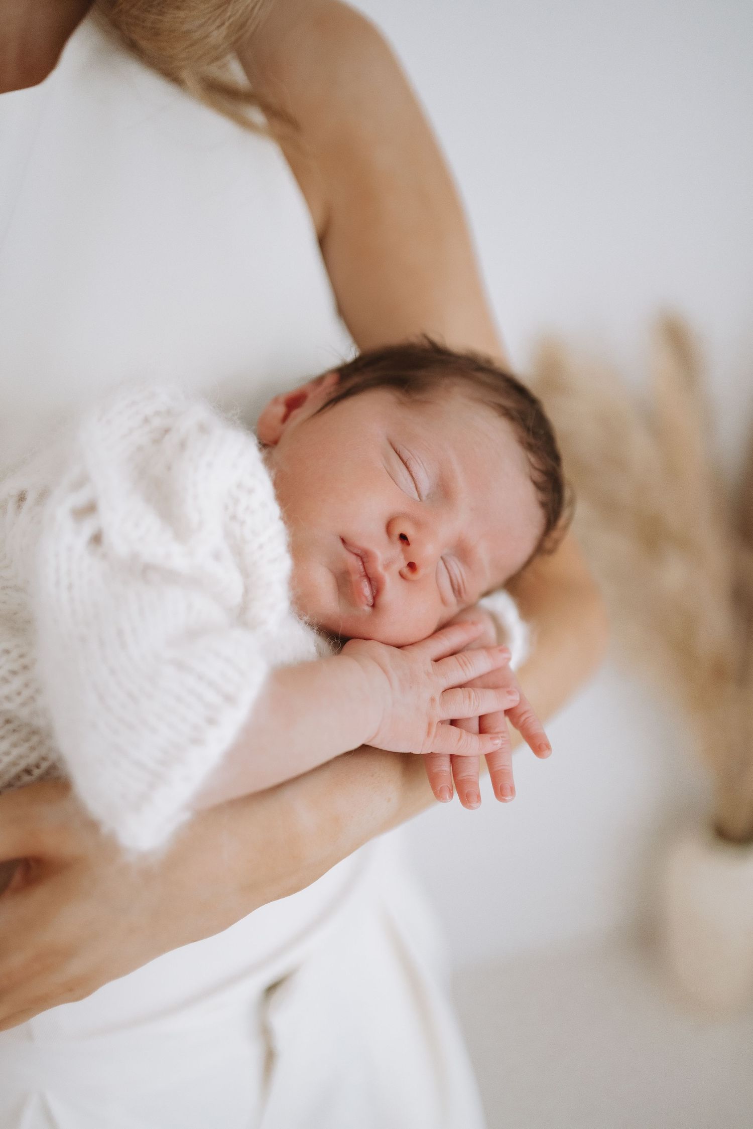 Sleeping newborn baby wrapped in soft white blanket rests peacefully in gentle natural light.