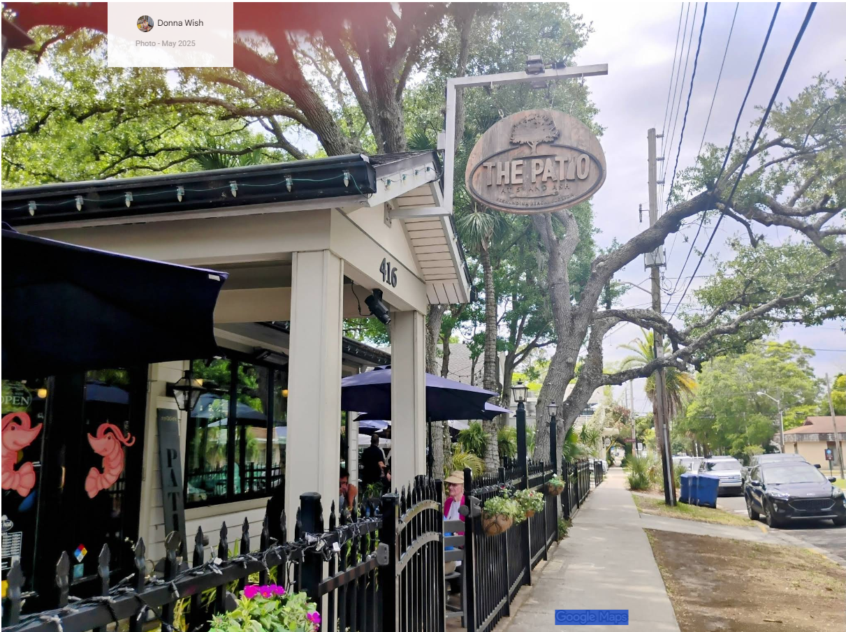 The Patio restaurant exterior with outdoor seating under oak trees on a rainy Florida street.