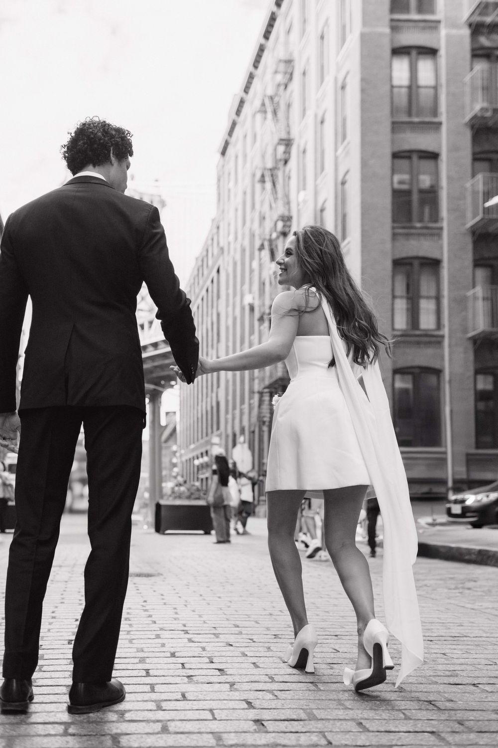 Black and white photos of couple walking on cobblestone street in urban setting.