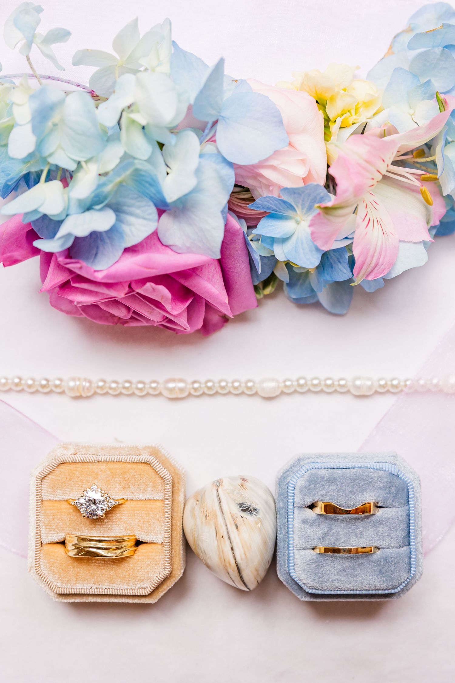 Delicate wedding ring boxes in peach and blue velvet with pastel floral decorations and pearl trim.