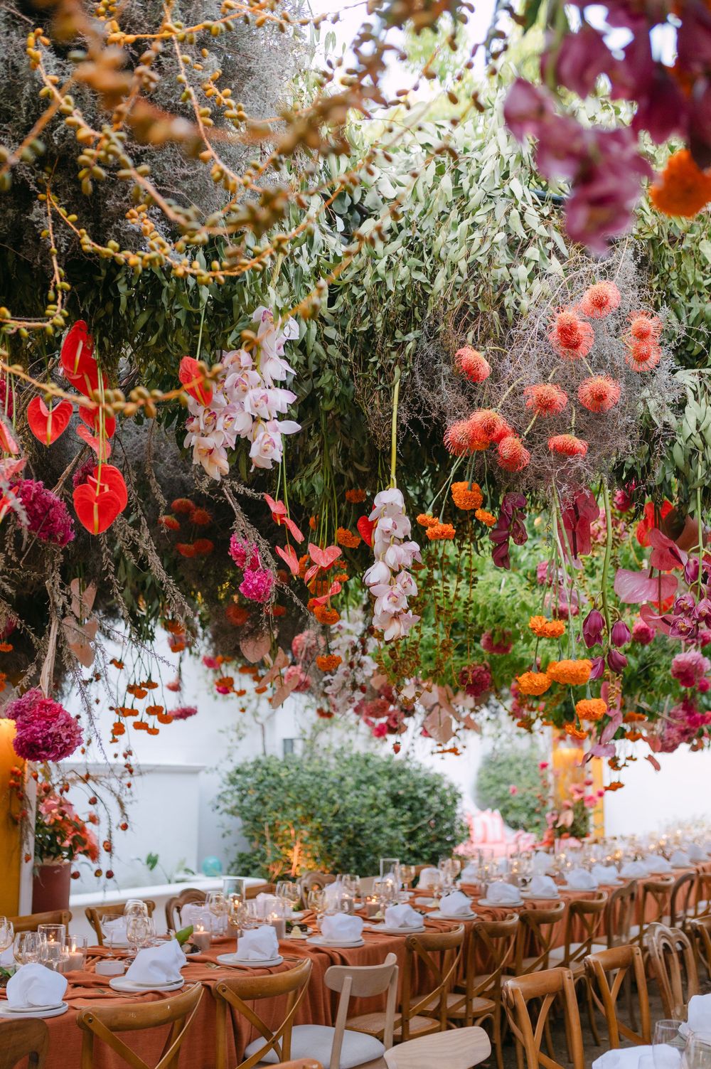 Elegant wedding reception table setup with hanging floral arrangements featuring orange and pink blooms under rustic decor.