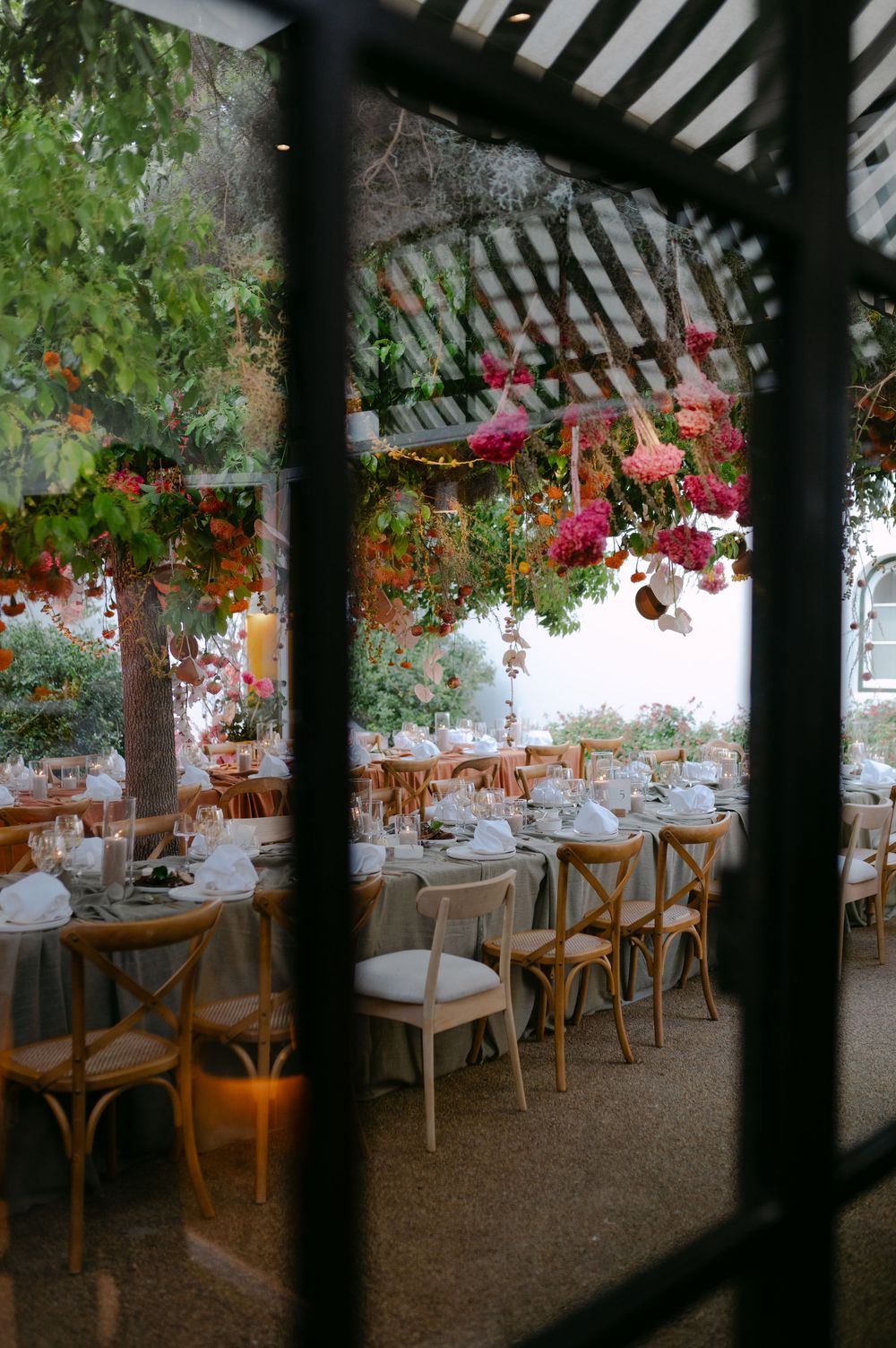 Wedding reception dining area with wooden cross-back chairs and dramatic overhead floral installations.