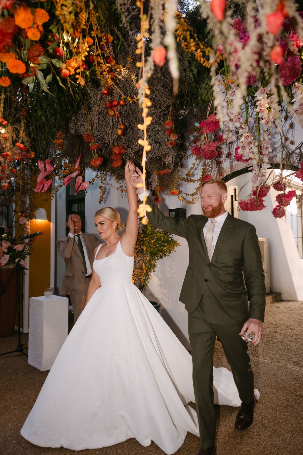 Wedding celebration under hanging floral decorations with string lights creating a magical atmosphere.