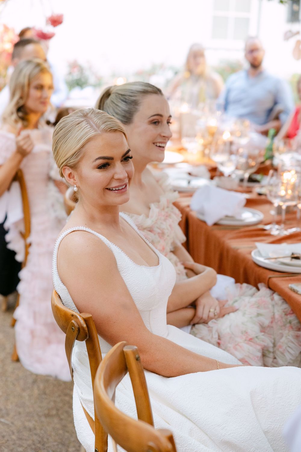 Wedding guests seated at an elegant outdoor reception table with white linens and gold chairs.