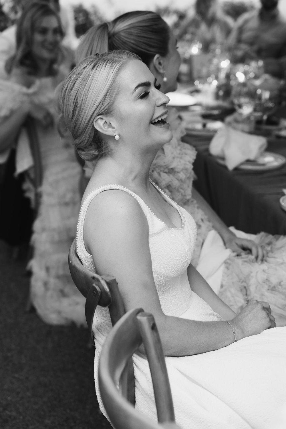 Black and white candid photo capturing joyful laughter during an elegant wedding reception.