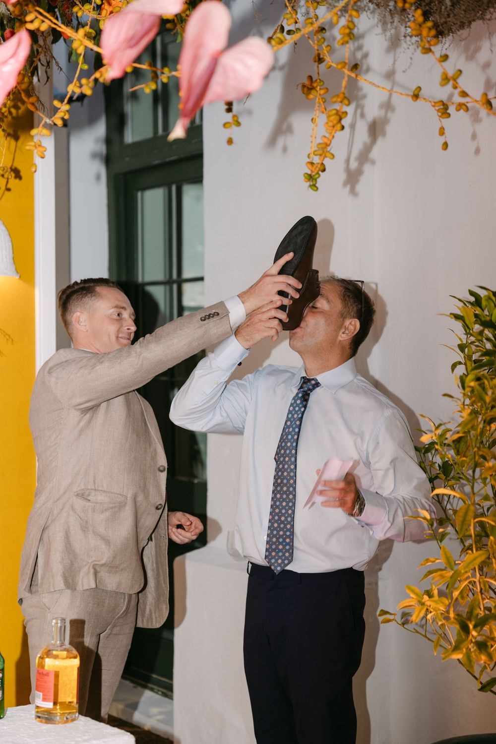 Wedding guests taking celebratory shots at a reception with yellow and pink decor.