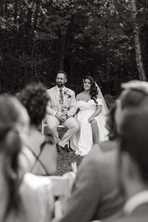 Black and white photo of wedding guests watching a couple dance during an outdoor forest reception.