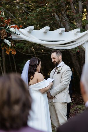 A romantic wedding ceremony moment under a flowing white canopy surrounded by autumn trees.