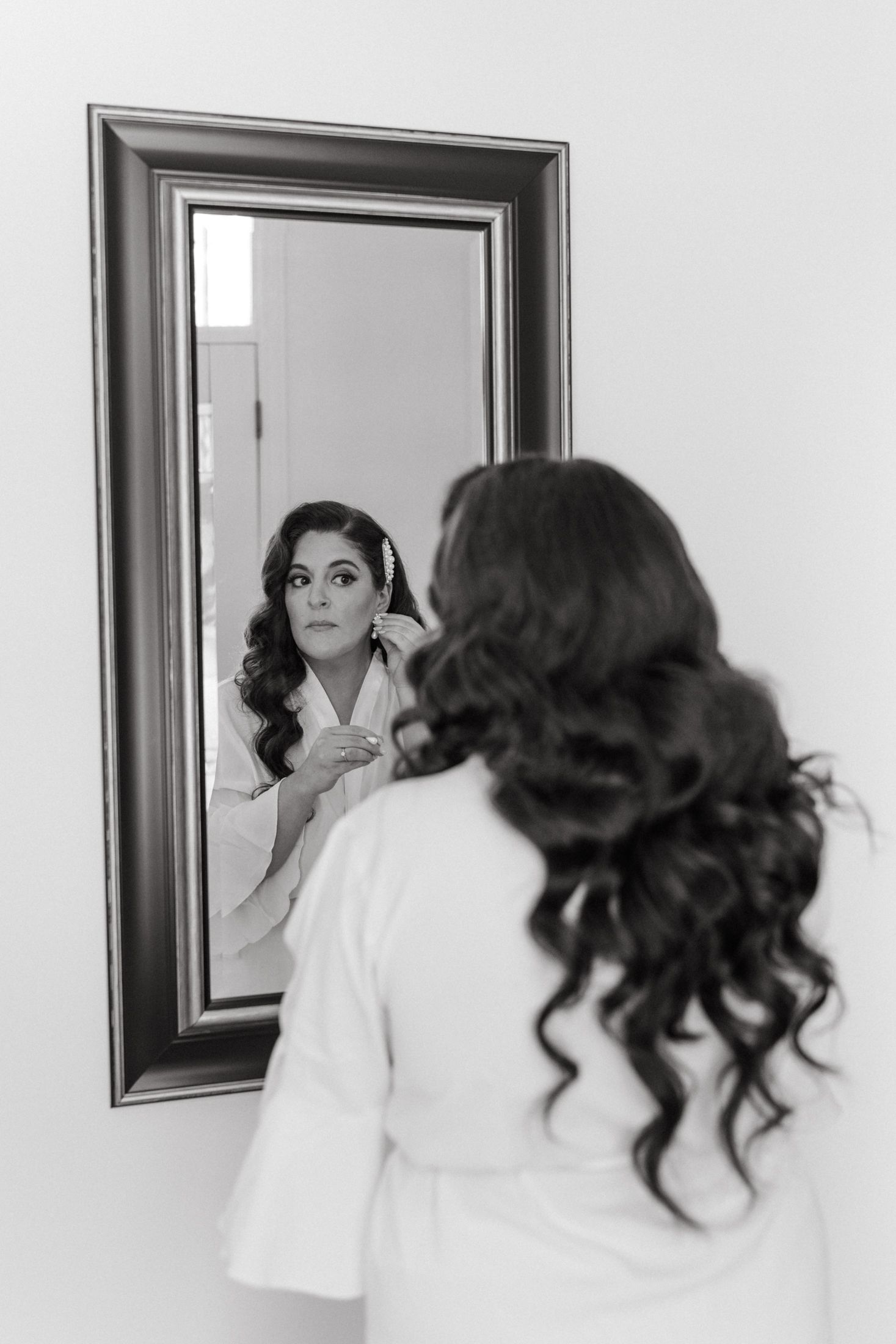 Black and white photo series showing someone in a white robe applying makeup while looking in a mirror.
