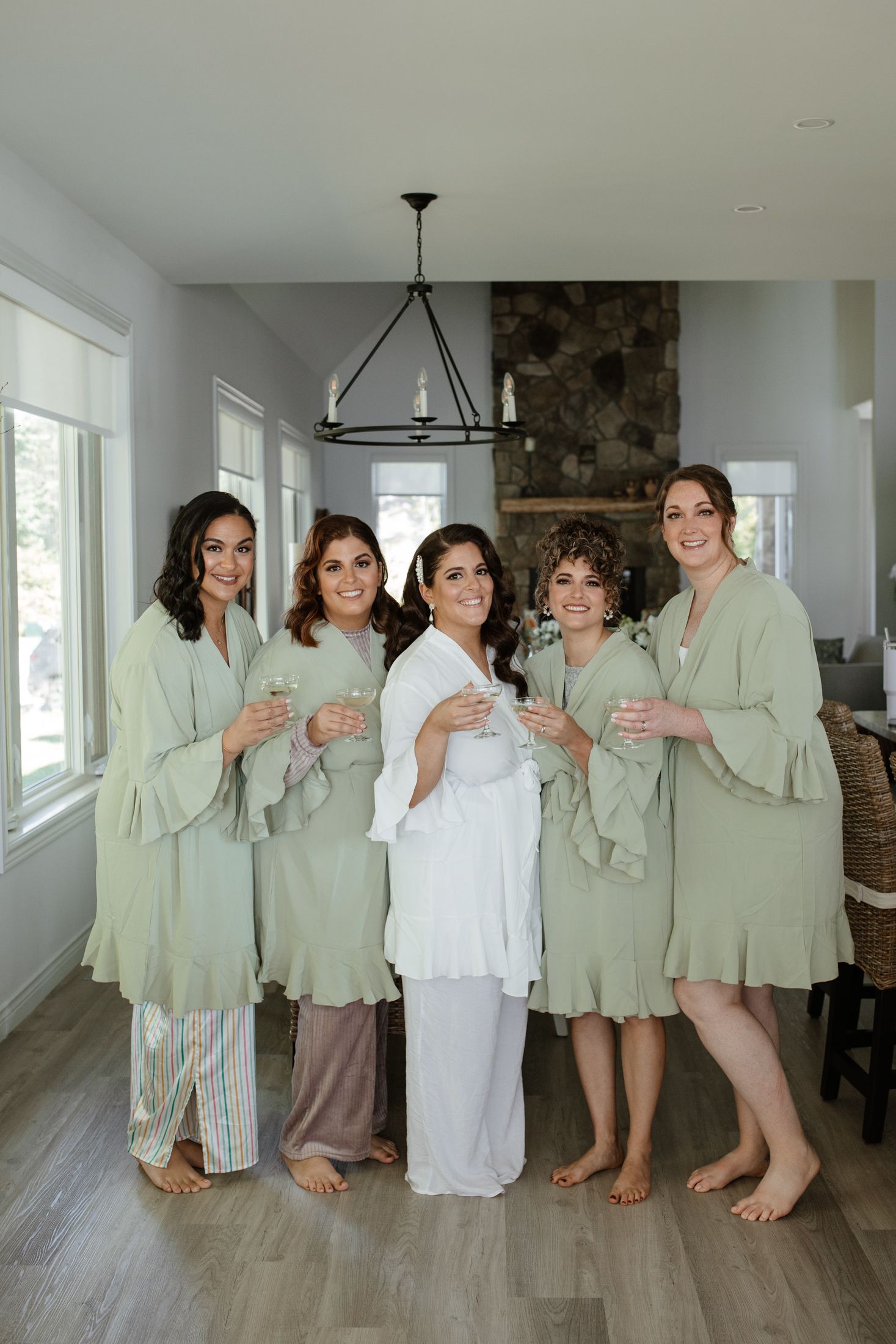 A group wearing matching sage green robes poses together on a light wood floor in a bright interior space.
