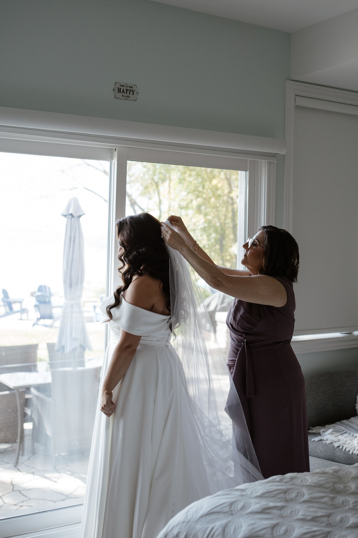 Wedding preparations show figures in white and purple dresses looking out bright windows in a modern room.