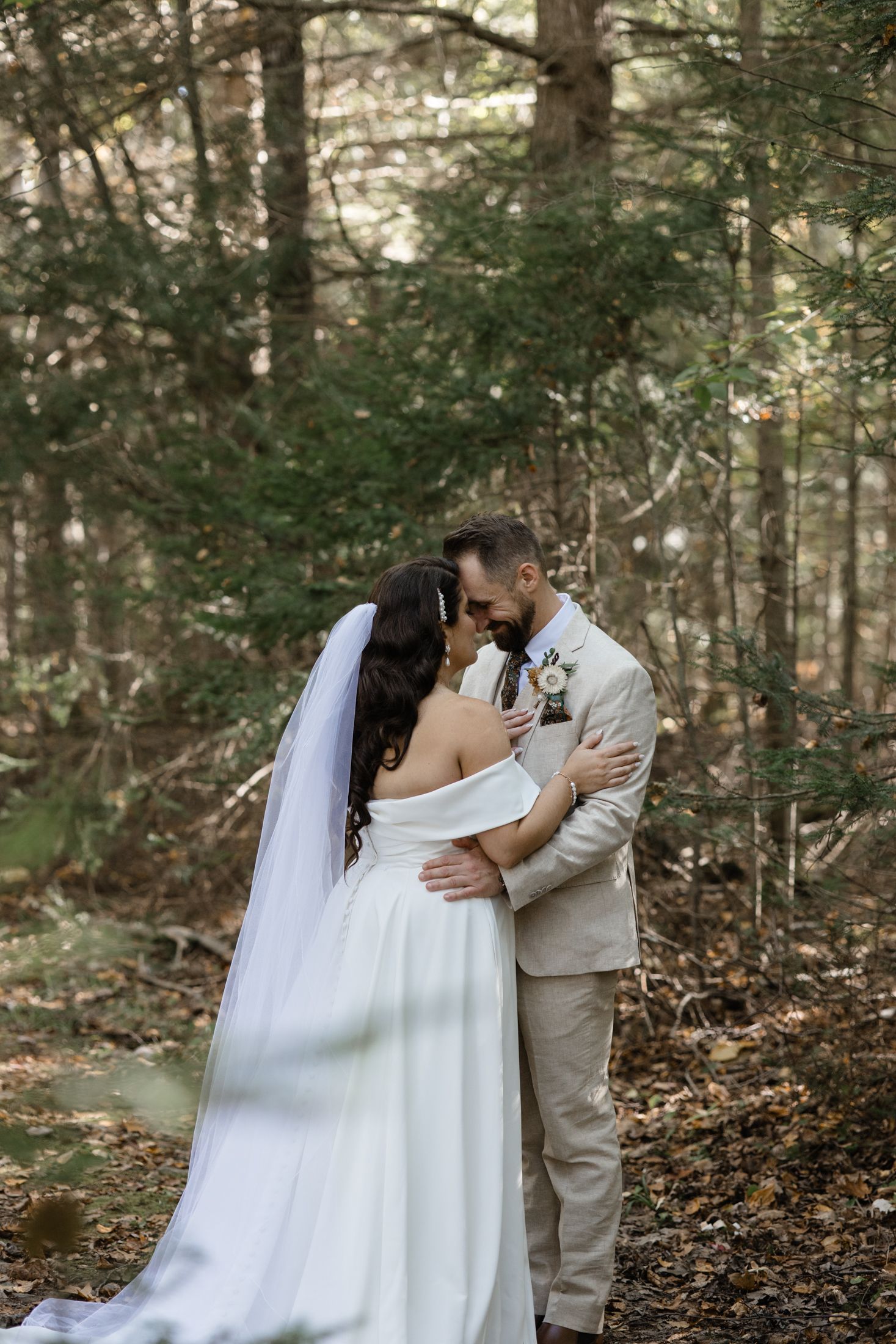 Romantic wedding couple shares intimate moments in a wooded forest setting with sunlight filtering through trees.