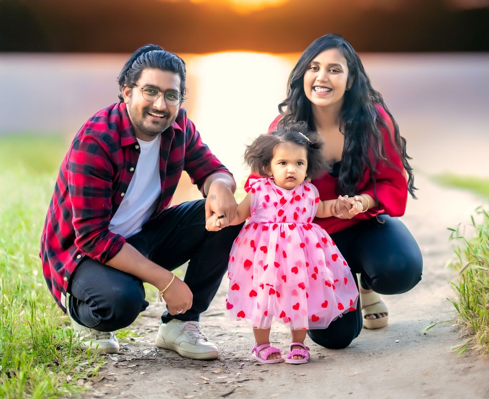 A couple crouches together outdoors during sunset while wearing red plaid and pink heart patterns.