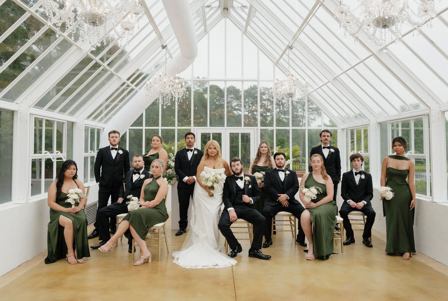 Wedding party poses in a bright conservatory with glass ceiling and chandeliers.