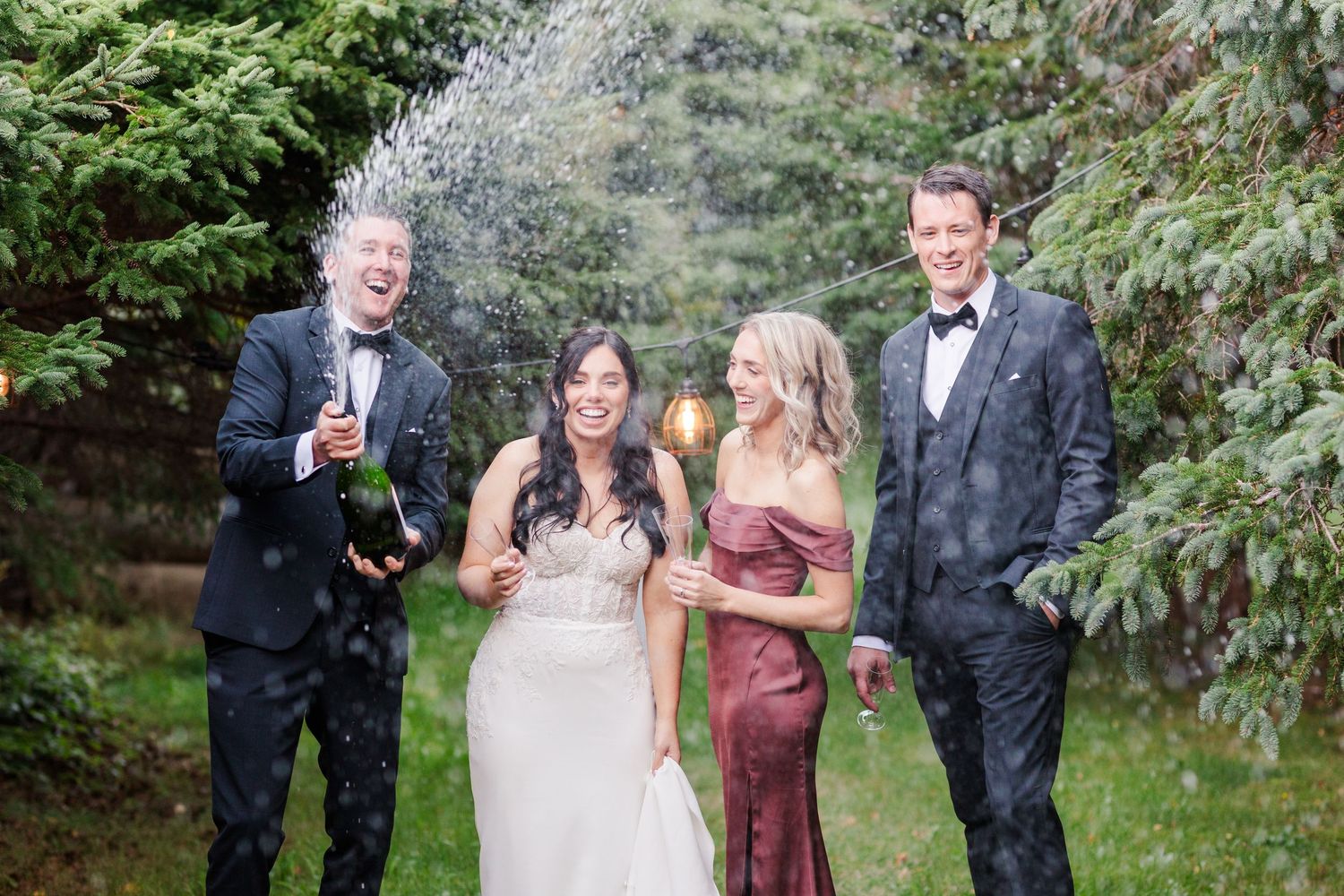 A wedding party enjoys celebratory toasts and laughter in a lush garden setting during an outdoor reception.