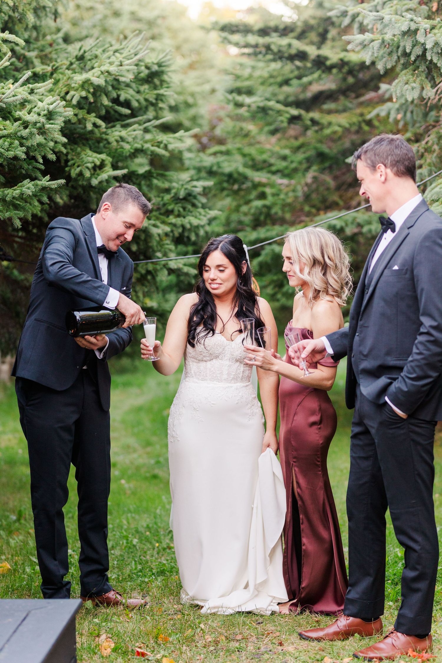 A wedding party laughs together while posing for candid photos outdoors in a garden setting.