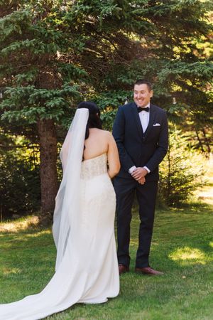 First look wedding photos of couple meeting in garden with flowing white dress and black tuxedo in summer setting.