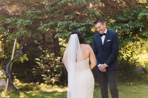 Couple in wedding attire holding hands during outdoor forest ceremony with sunlight filtering through trees.