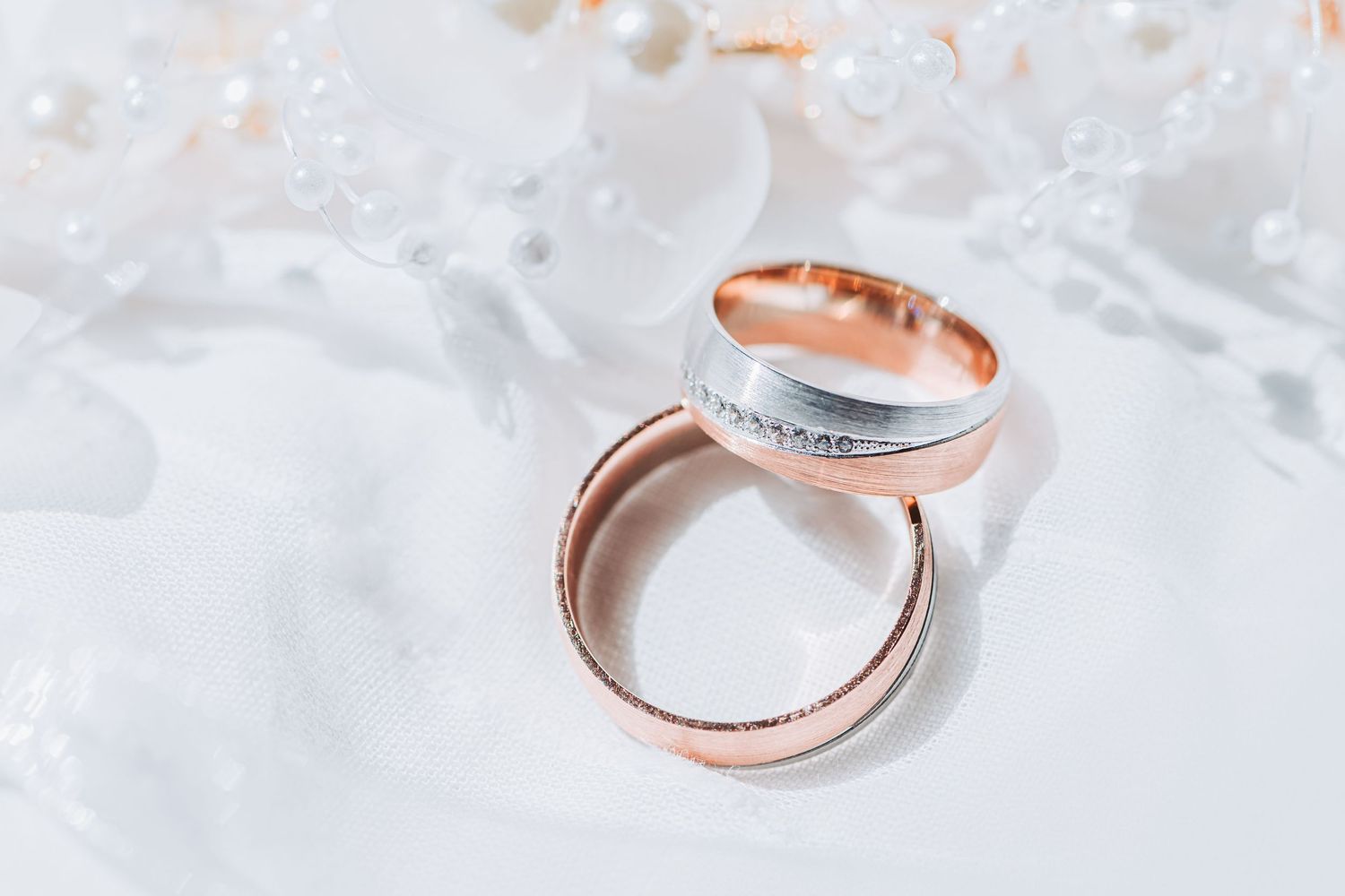 Two elegant wedding rings in rose gold and silver tones displayed on a white marble surface.
