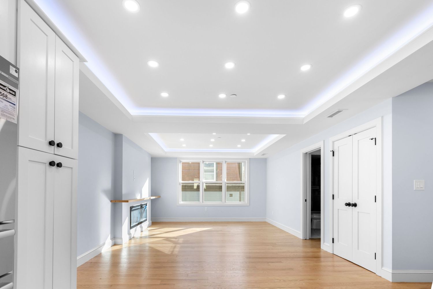Bright open living space with tray ceiling, LED lighting, hardwood floors, and a fireplace.