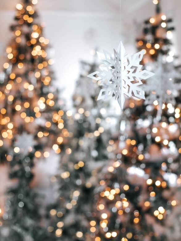 A cozy Christmas scene with a decorated fireplace, flocked wreath, red curtains, and a lit white Christmas tree.