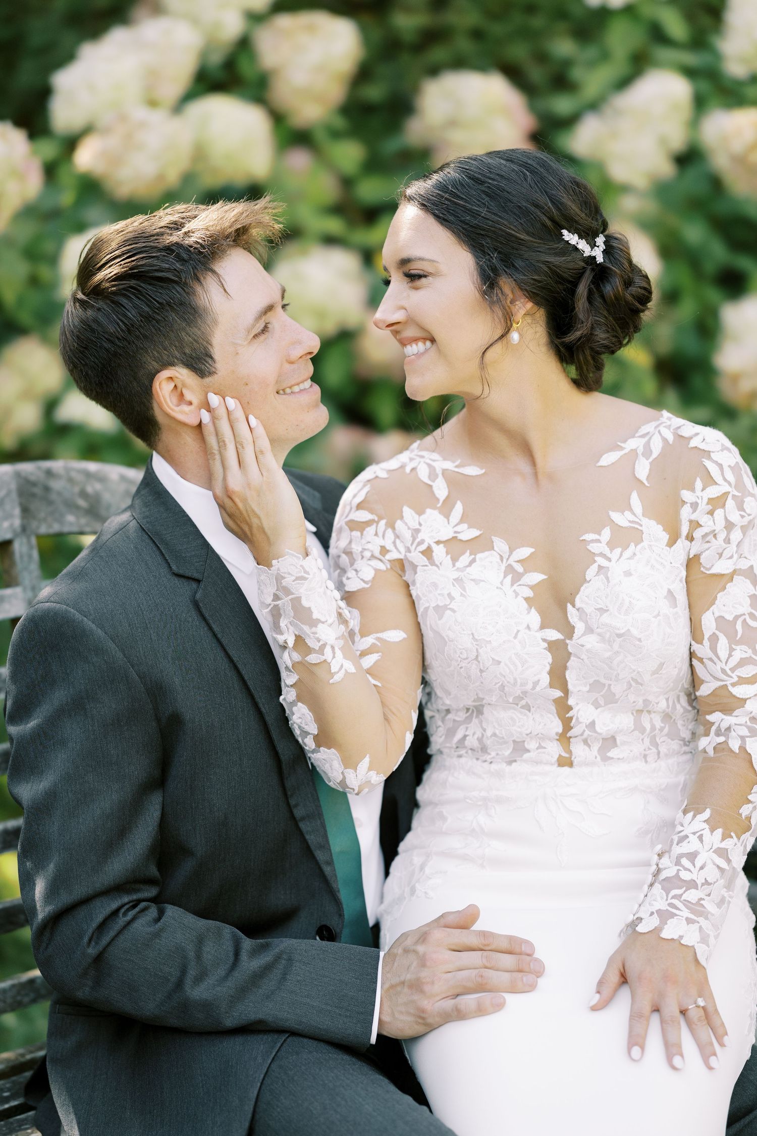 A romantic wedding couple shares intimate moments in a garden setting with white flowers in the background.