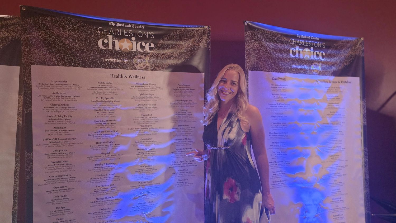 A person stands next to a large banner display with pink and teal lighting effects at an event venue.