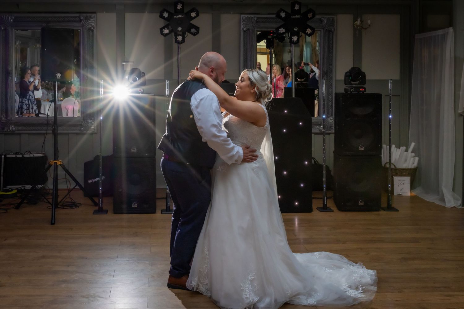 A couple shares a romantic dance at their wedding reception as camera flashes illuminate the dimly lit ballroom.