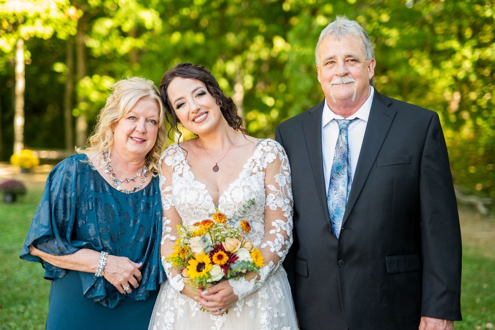 Wedding party members in formal attire pose together outdoors on a sunny day.