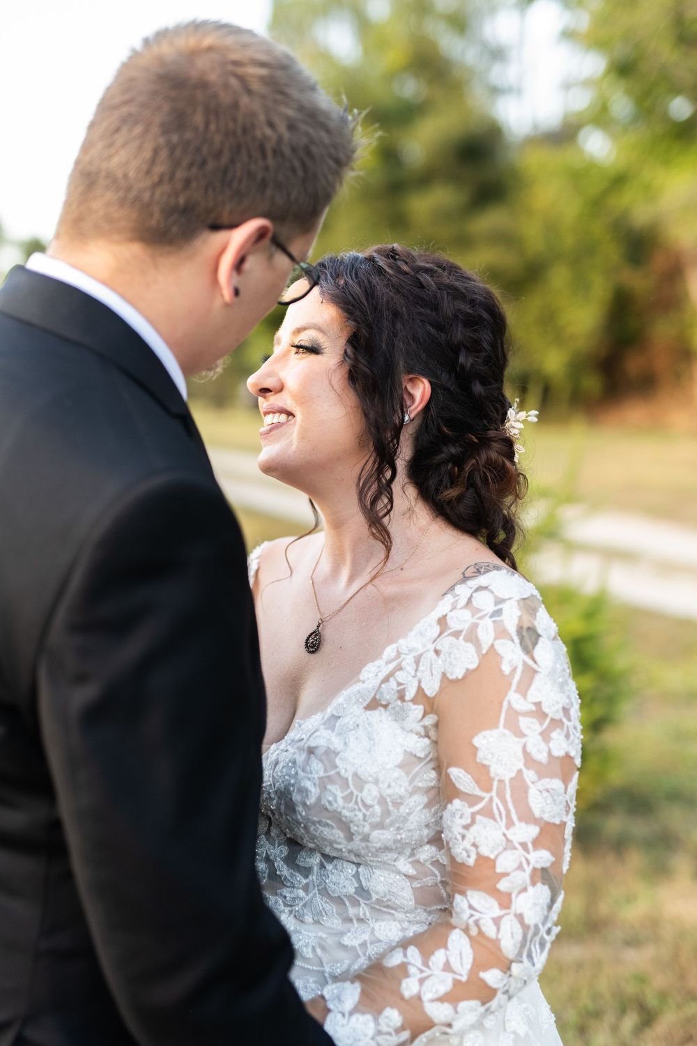 A couple in wedding attire shares a romantic moment outdoors with laughter and joy in a natural setting.
