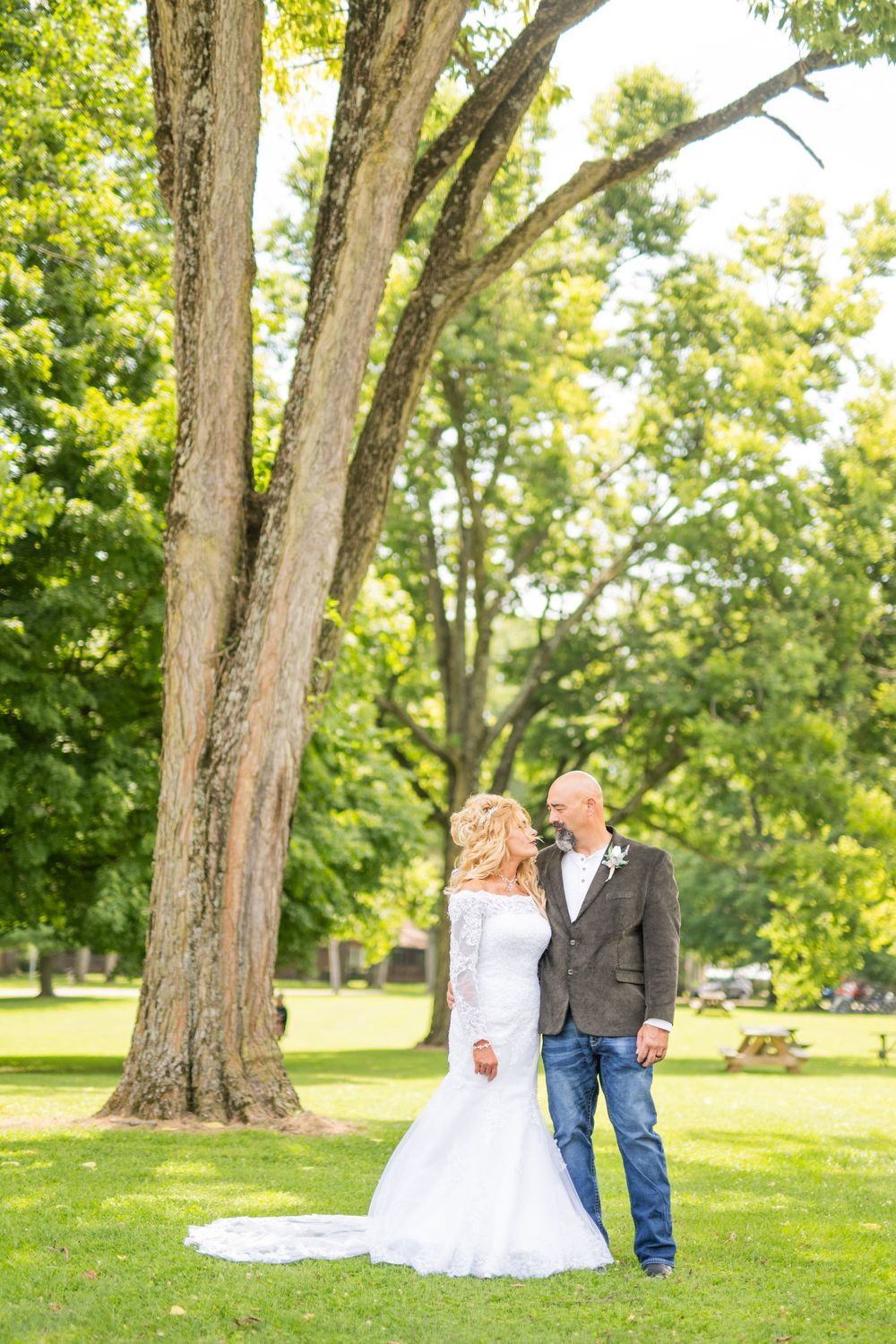 Wedding photography sequence showing couple posing under mature trees in park setting.