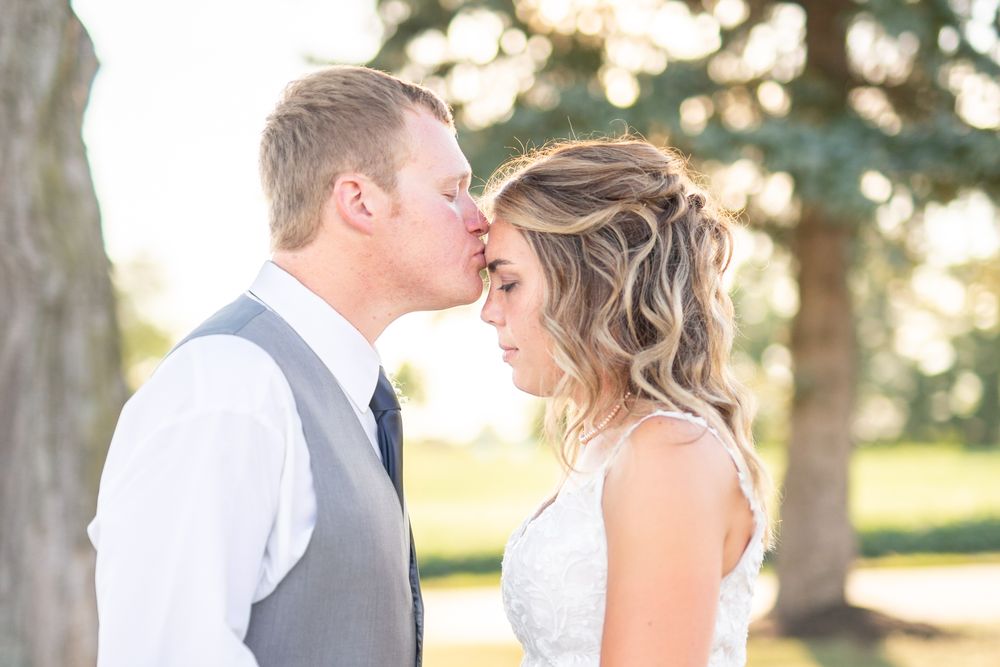 Romantic wedding couple embraces in a sunlit outdoor setting with flowing white dress and grey suit.