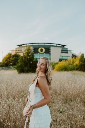 A person celebrates graduation with energetic poses near the Oregon Ducks stadium.