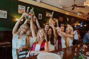 Friends raise glasses in toast at bar with green walls and vintage decor.