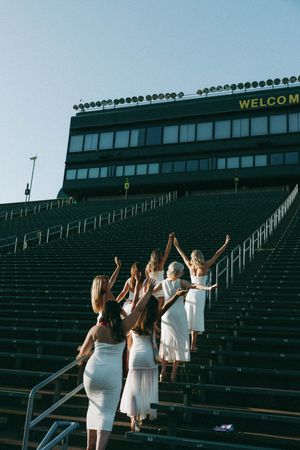 Group in white dresses ascending stadium bleacher steps under Welcome sign at sunset.