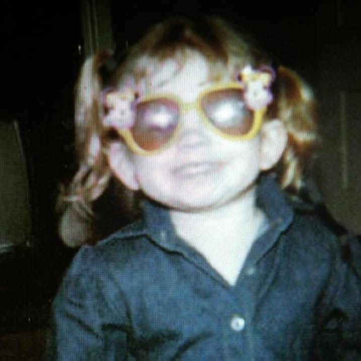 Child wearing sunglasses and dark shirt in vintage-style photograph.
