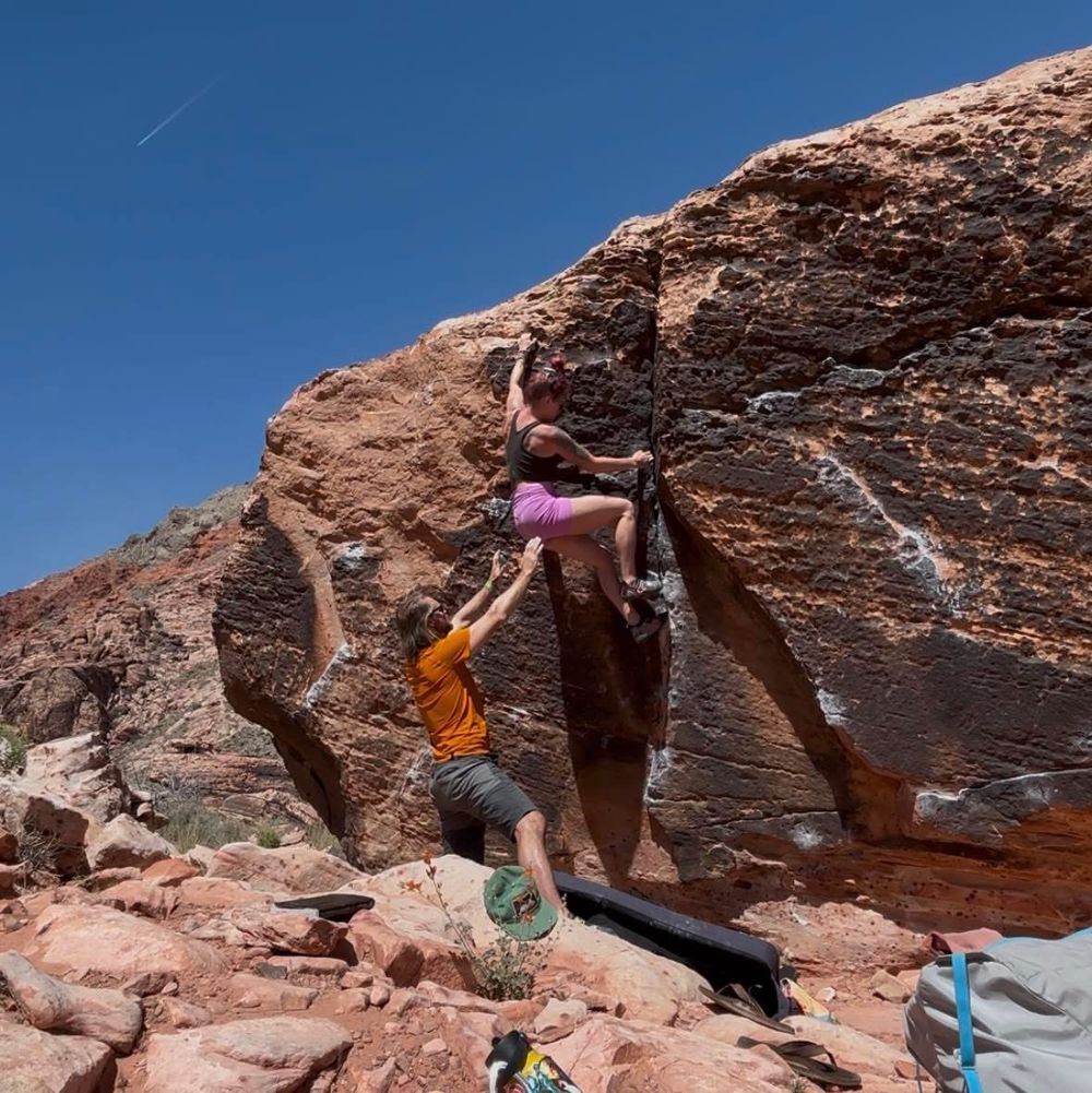 Rock climber scaling red rock face wearing pink and orange gear.